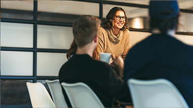 A woman, standing, commanding a table of her peers, seated.